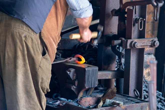 Коваль у майстерні обробляє розпечений метал на ковадлі