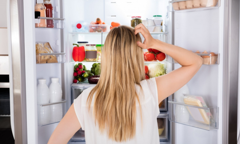 На фото жінка стоїть перед відкритим холодильником