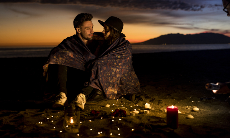 Молода пара у ковдрі сидить на березі моря, фото