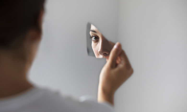 Женщина смотрит в разбитое зеркало.