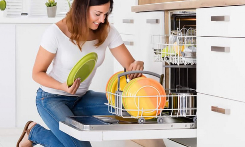 На фото женщина складывает посуду в посудомойку.